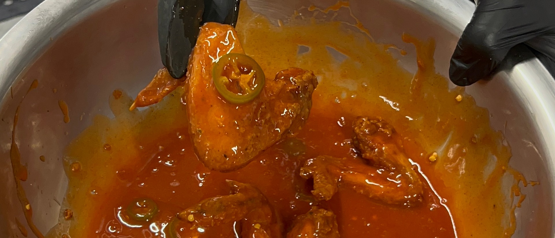 Buffalo-sauced wing with a jalapeño slice lifted from the sauce bowl with tongs